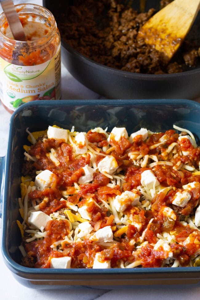 Dorito, meat and cheese mixture covered with salsa in baking dish.