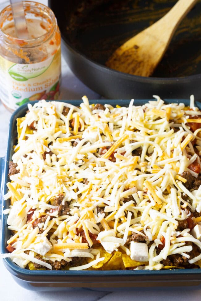 Baking dish with Dorito mixture topped off with shredded cheese layer.