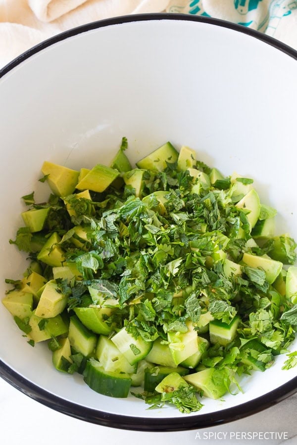Bowl filled with avocado, cucumber and herbs.