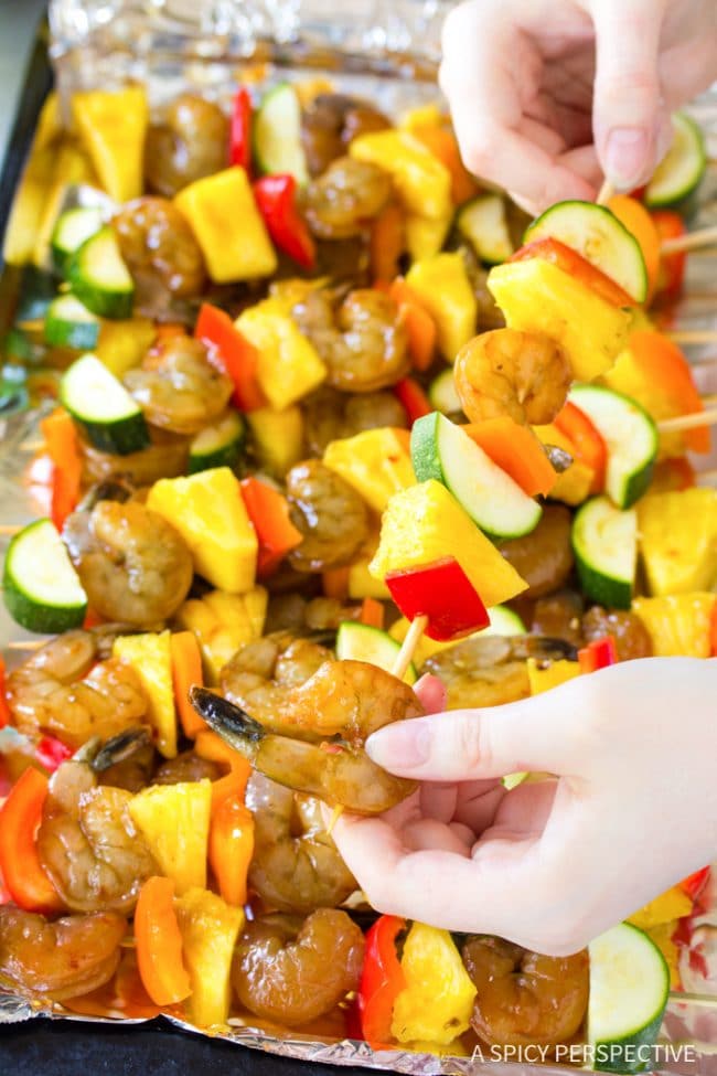 Closeup of hand skewering shrimp and vegetables onto wooden skewers. 