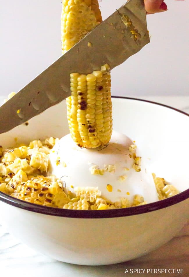 Closeup of a knife removing corn kernels from the cob into a bowl.