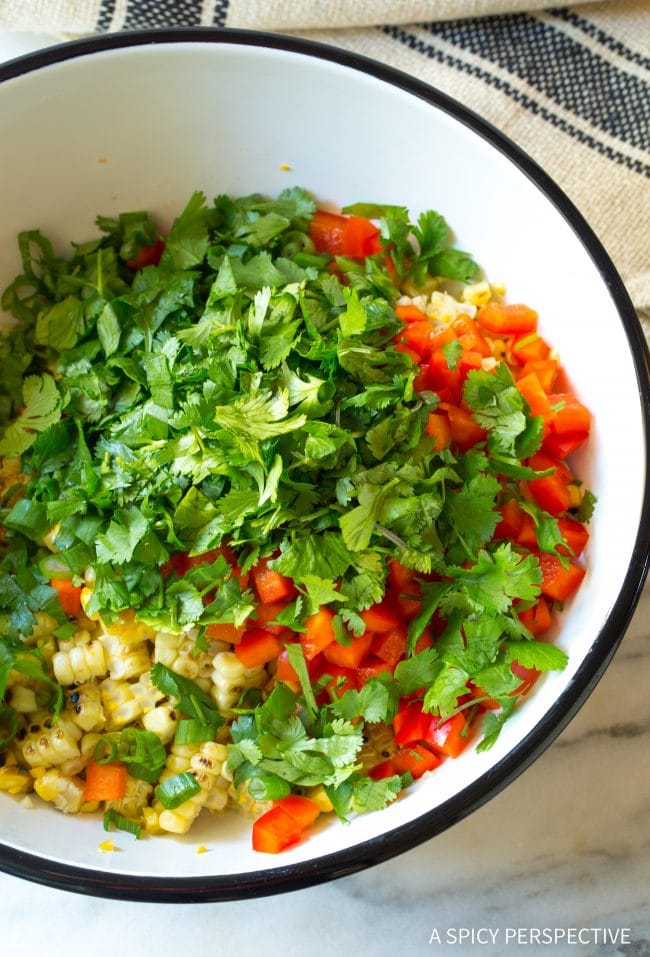 Overhead of a bowl filled with ingredients for street corn salad - cilantro, red bell pepper, corn, green onions.