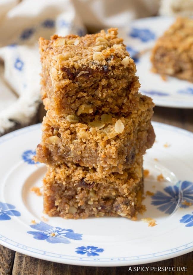 Breakfast oatmeal bar recipe cut and stacked on a plate with nuts and dates visible.