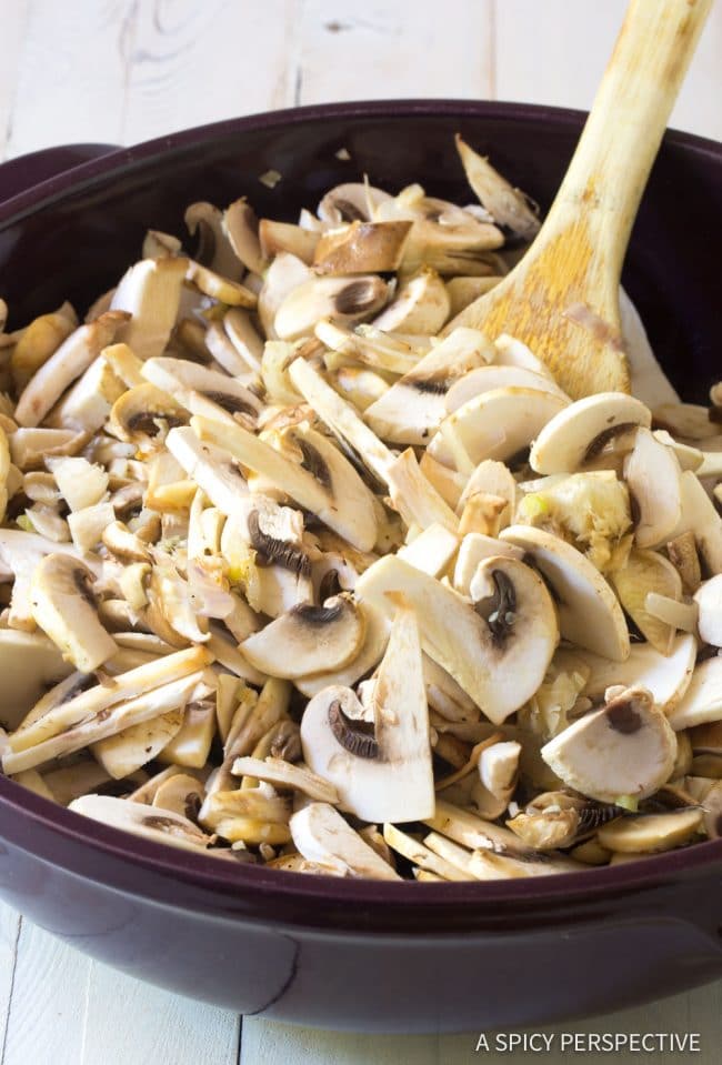Raw sliced mushrooms in a pan with a wooden spoon.