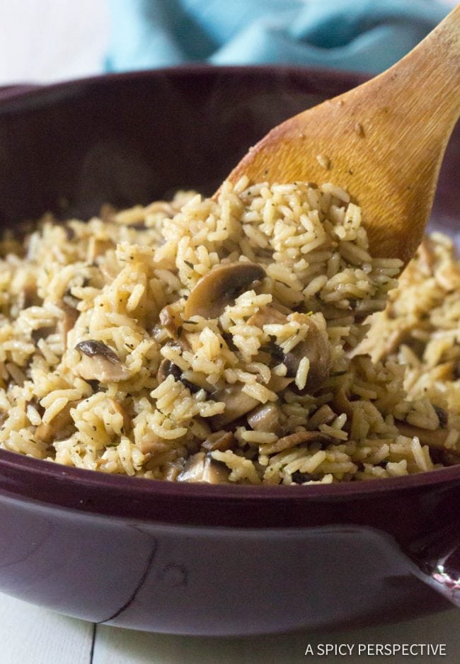 Cooked mushroom rice pilaf in a pan being stirred by a wooden spoon.