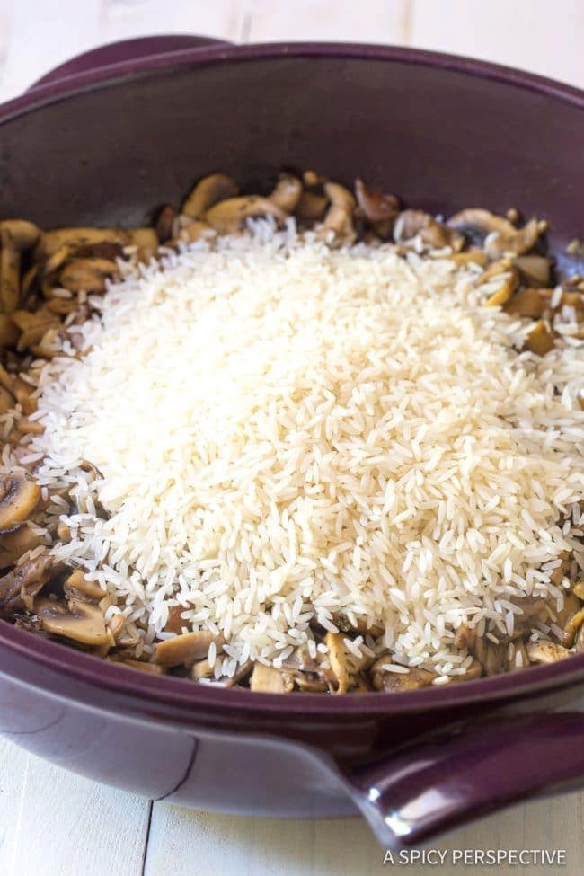 Sauteed mushrooms in a pan topped with uncooked rice.
