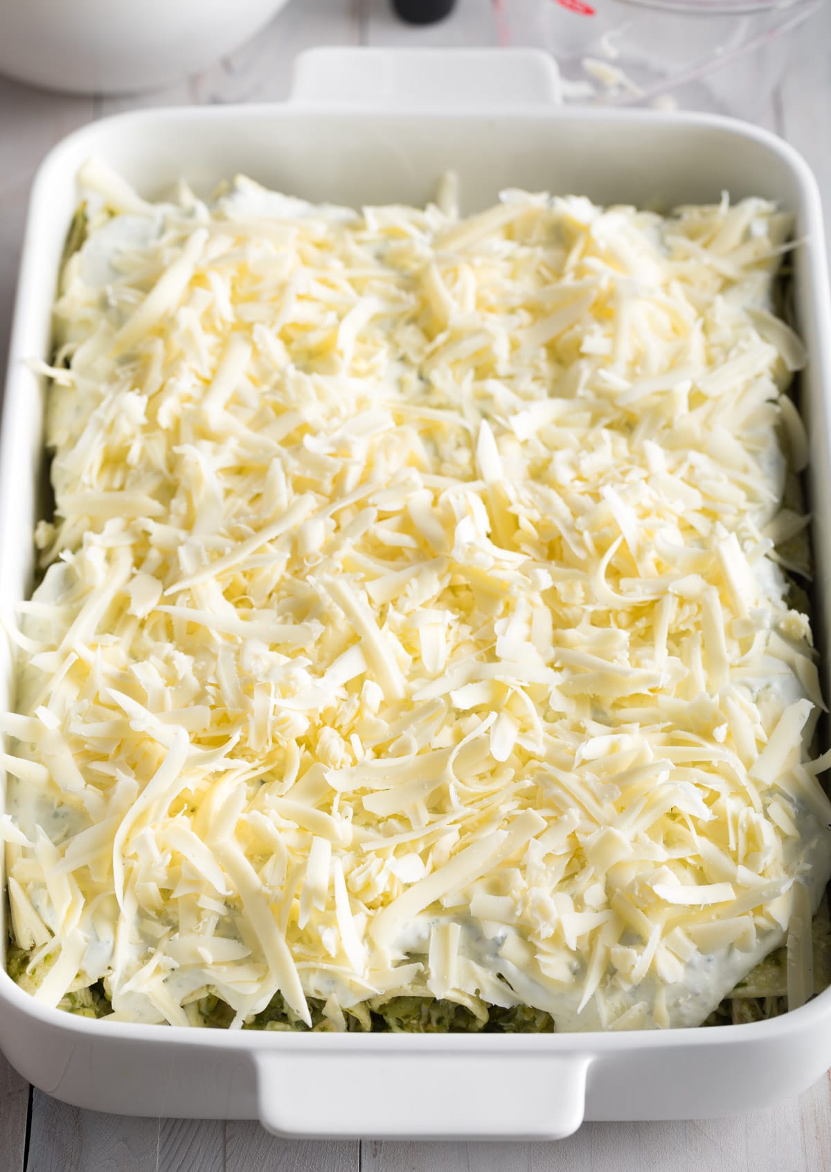 Tray filled with enchiladas that are topped off with cream and shredded cheese ready to bake. 