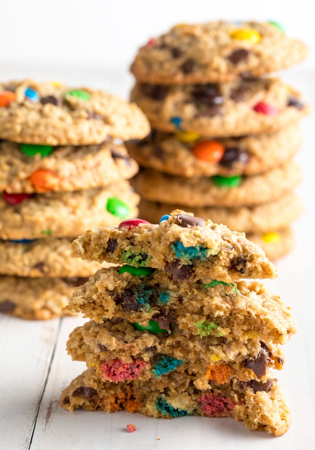 Three sets of 6 peanut butter and oatmeal monster cookies with m&ms in a stack. The cookies in the closest stack have been broken in half to show the candies inside.