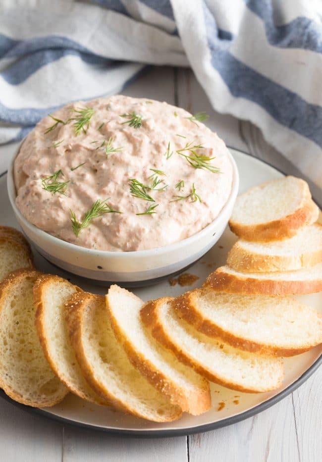 Small bowl filled with the smoked salmon dip with some toasted bread on the plate around it 
