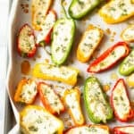 Colorful stuffed mini peppers with cheese and herbs on baking sheet.