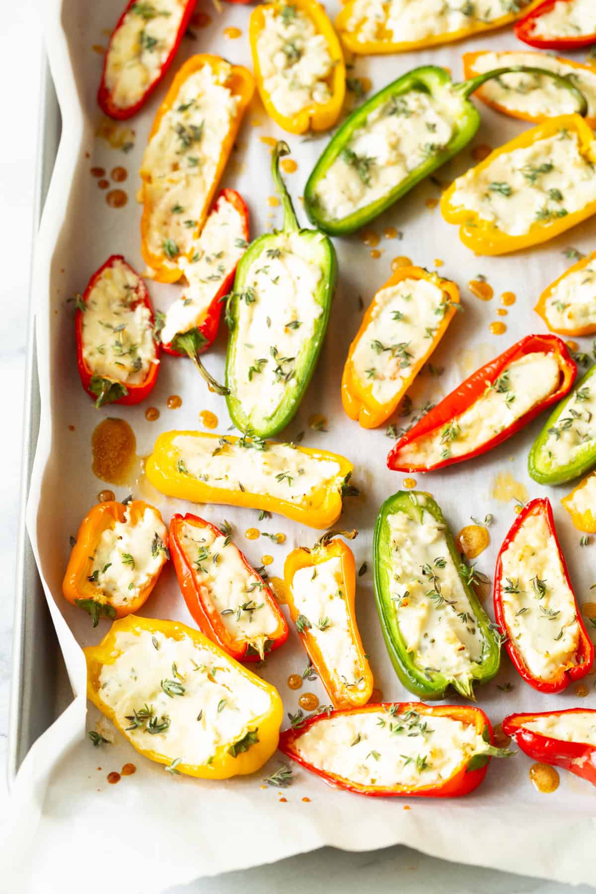 Colorful stuffed mini peppers with cheese and herbs on baking sheet.