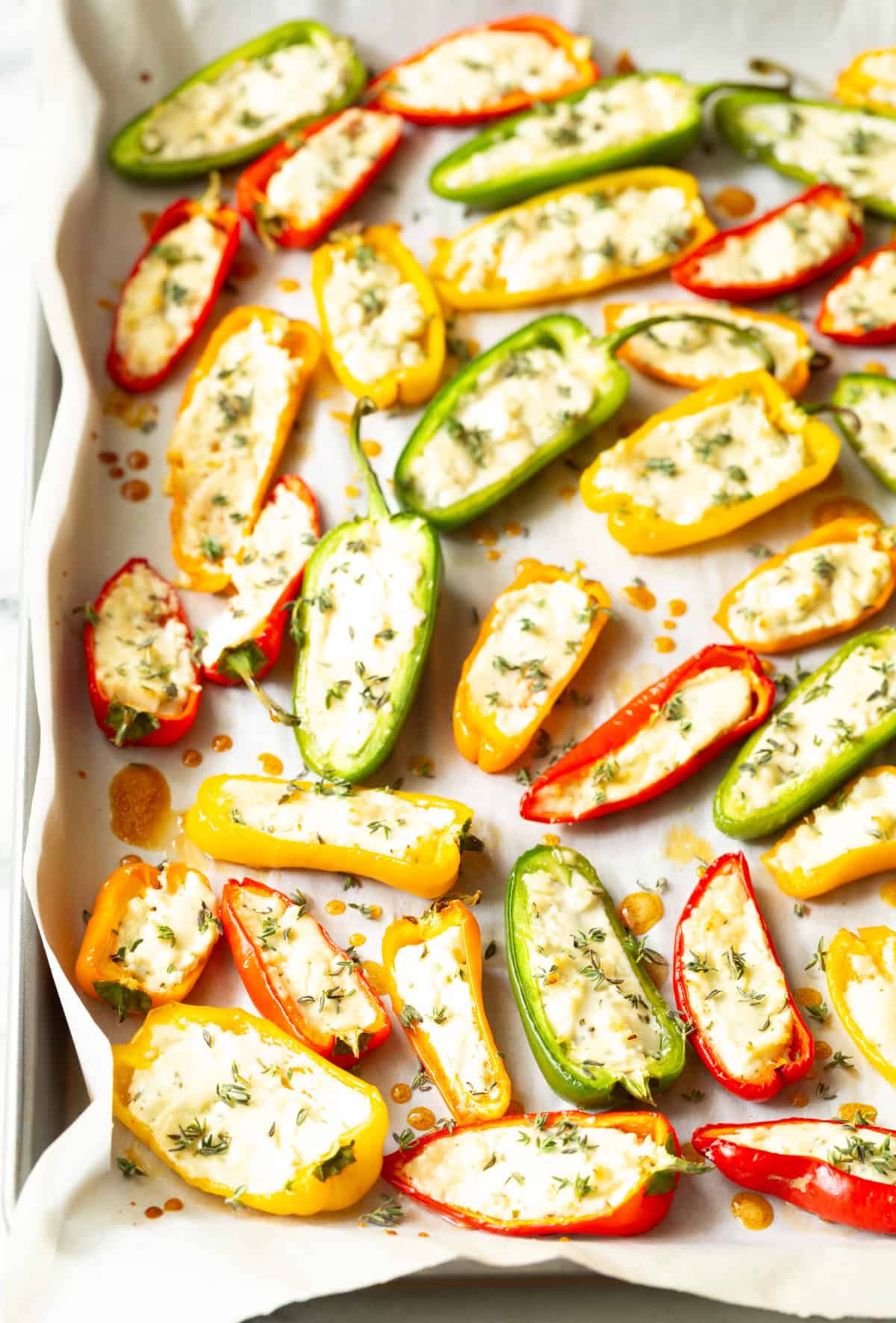 Colorful stuffed mini peppers with cheese and herbs on baking sheet.