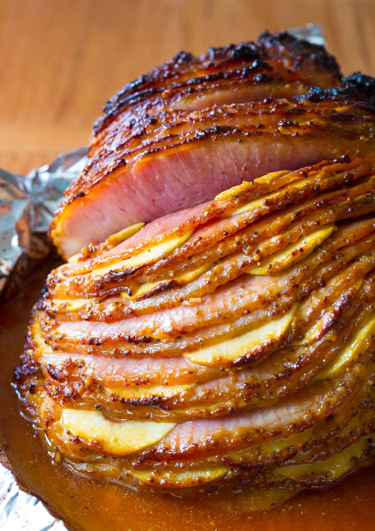 This Baked Ham Recipe is the perfect centerpiece to your holiday meal. Slathered with honey mustard ham glaze, stuffed with apples and baked to perfection! #ASpicyPerspective #Holiday # Easter #Christmas #Thanksgiving #Ham #BakedHame #BakedHamRecipe #HoneyMustard #Apples #HamGlaze Spiral cut ham with apples sliced in between the slices with a glaze on top.