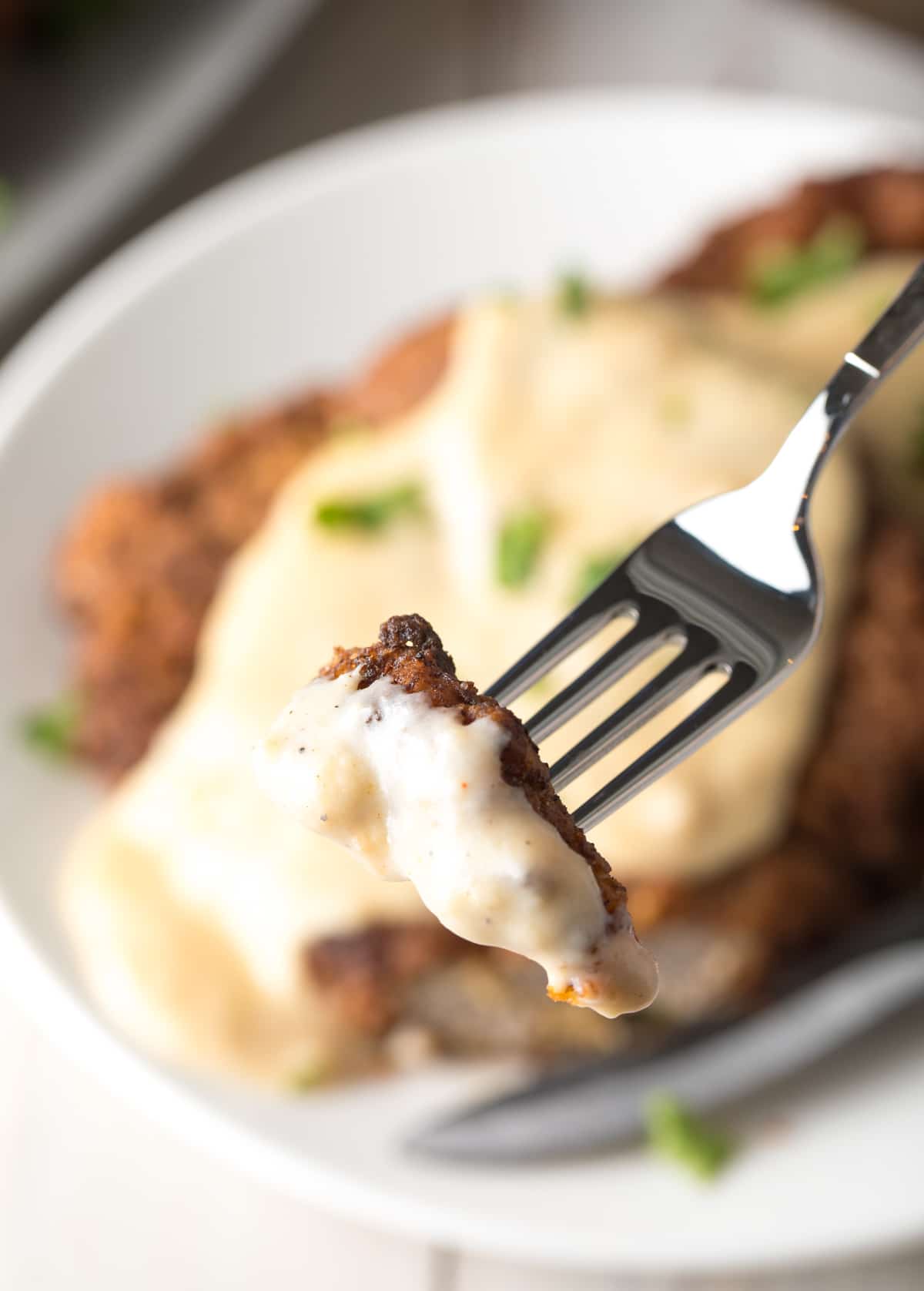 Fork holding a piece of chicken fried steak coated in gravy.
