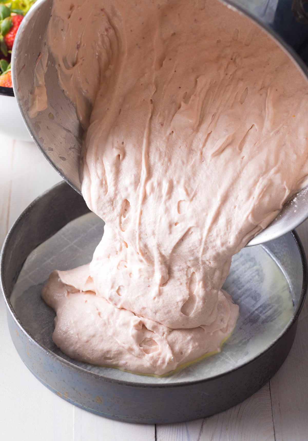 Cake batter being poured into greased cake pan. 