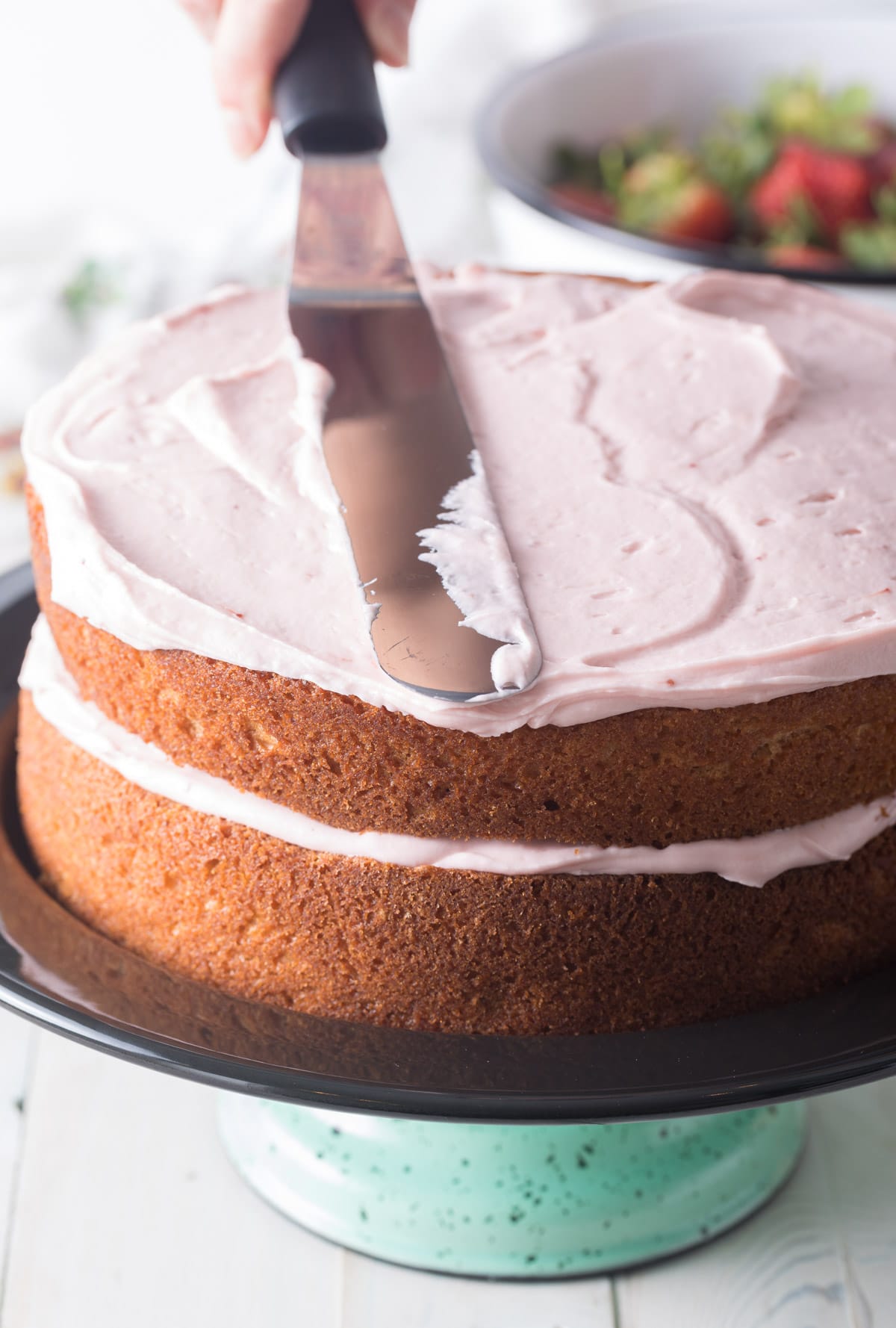 Hand spreading frosting over cake layers. 
