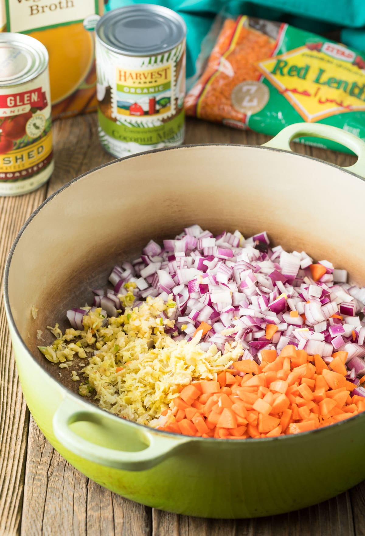 Large cooking pot filled with chopped red onion, chopped carrots and garlic.