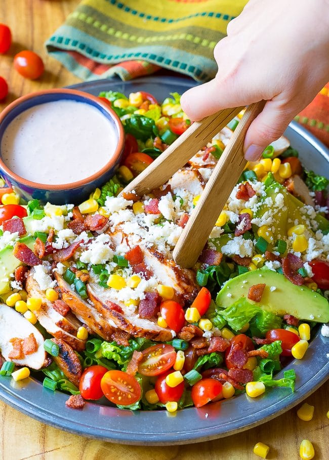 Hand is tossing the Mexican chicken salad in a bowl with wooden tongs.
