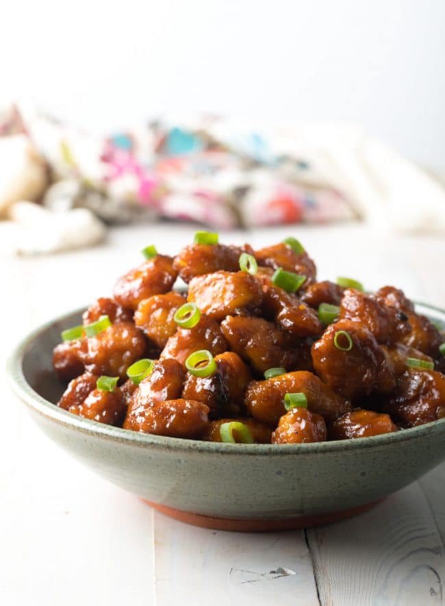 Side view of firecracker chicken in a bowl garnished with sliced scallions.