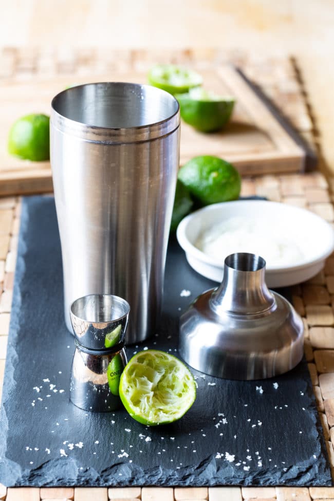 Sugar Rimmed Glass #ASpicyPerspective #Margarita #MargaritaRecipe #BestMargaritaRecipe #HowtoMakeaMargarita #Drink #Tequila #CincodeMayo #ClassicMargarita #Margaritas #Mexican #Cocktails Cocktail shaker next to a jigger and limes.