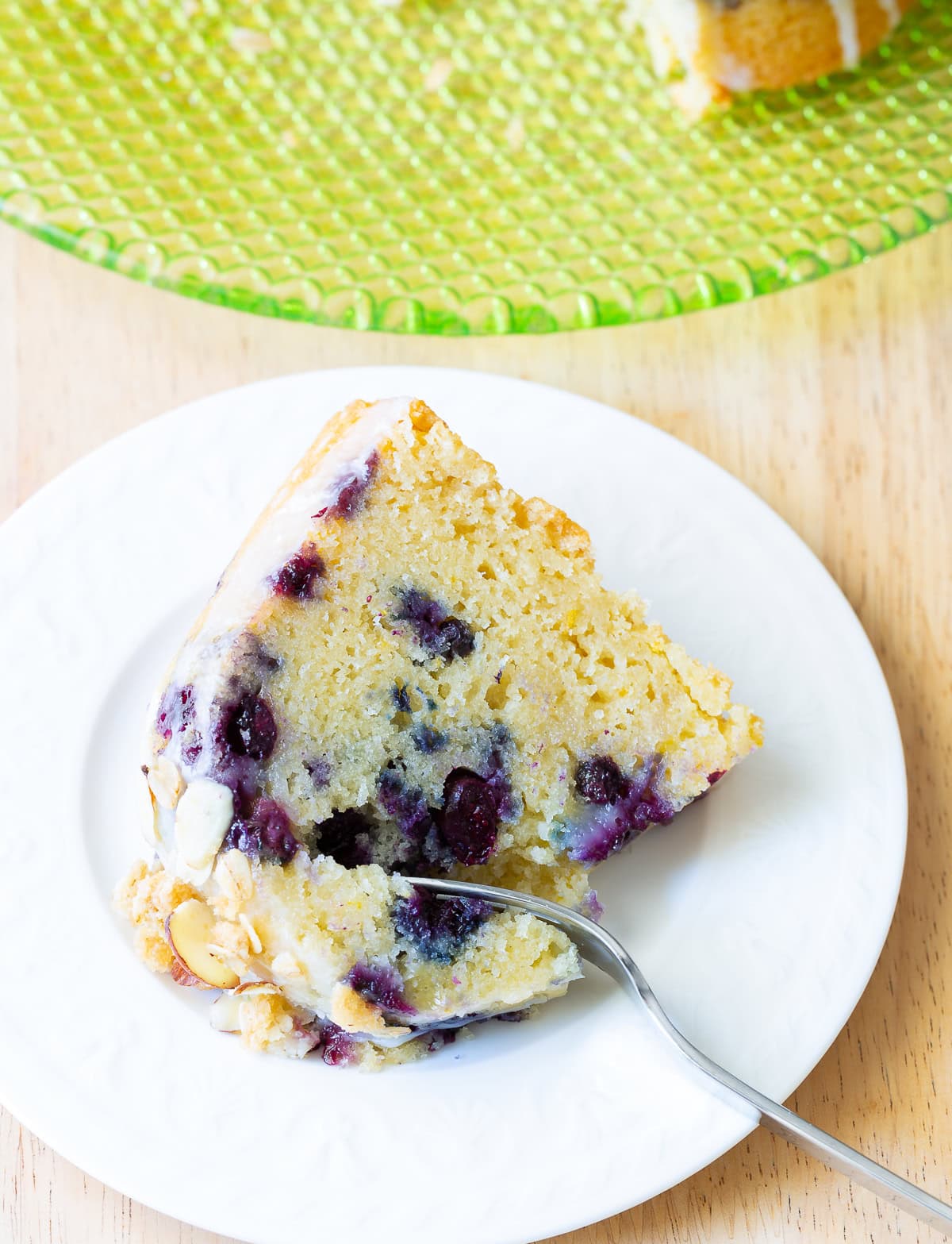 Slice of blueberry cake on a plate with a fork removing a part. 