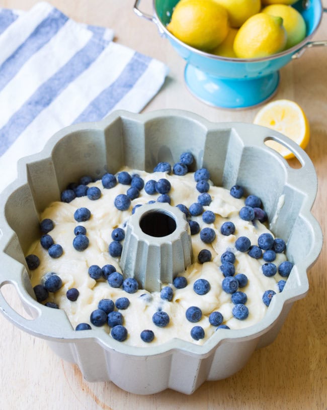 Blueberry cake batter in a prepared bundt pan with fresh blueberries sprinkled over the top. 