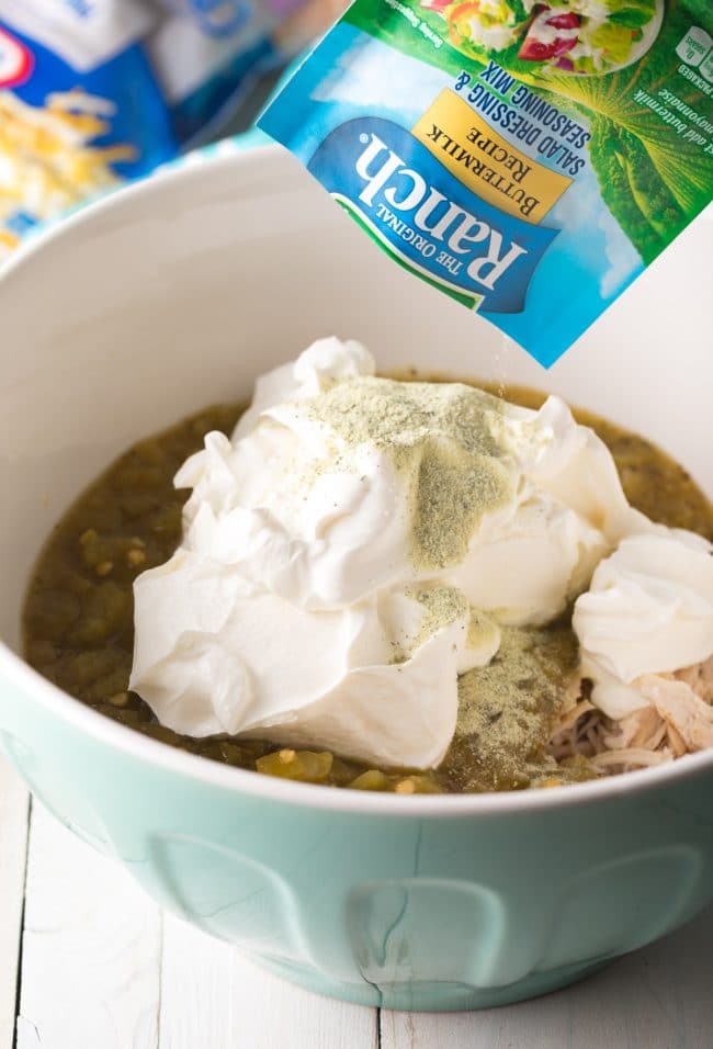 Adding sour cream and ranch dip mix to a large bowl with shredded chicken and salsa.