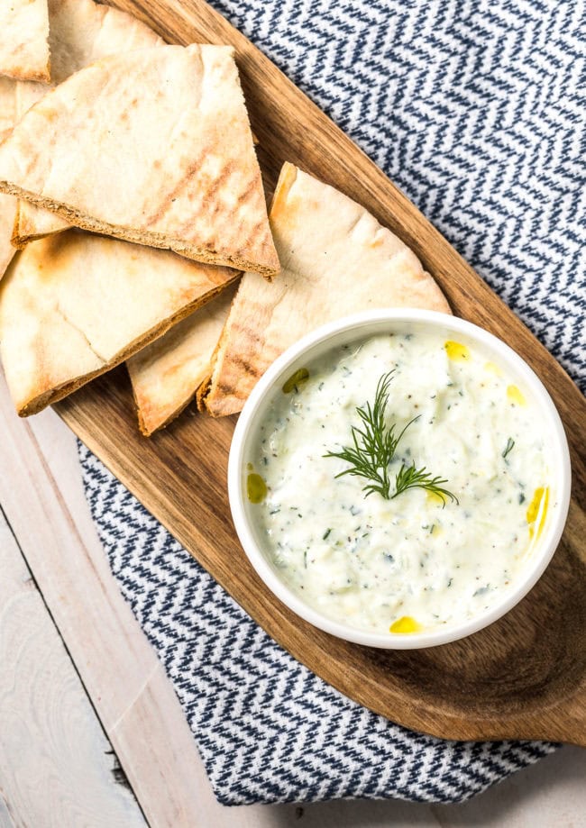 Tzatziki dip in a white bowl, placed on a wood platter with pita bread.