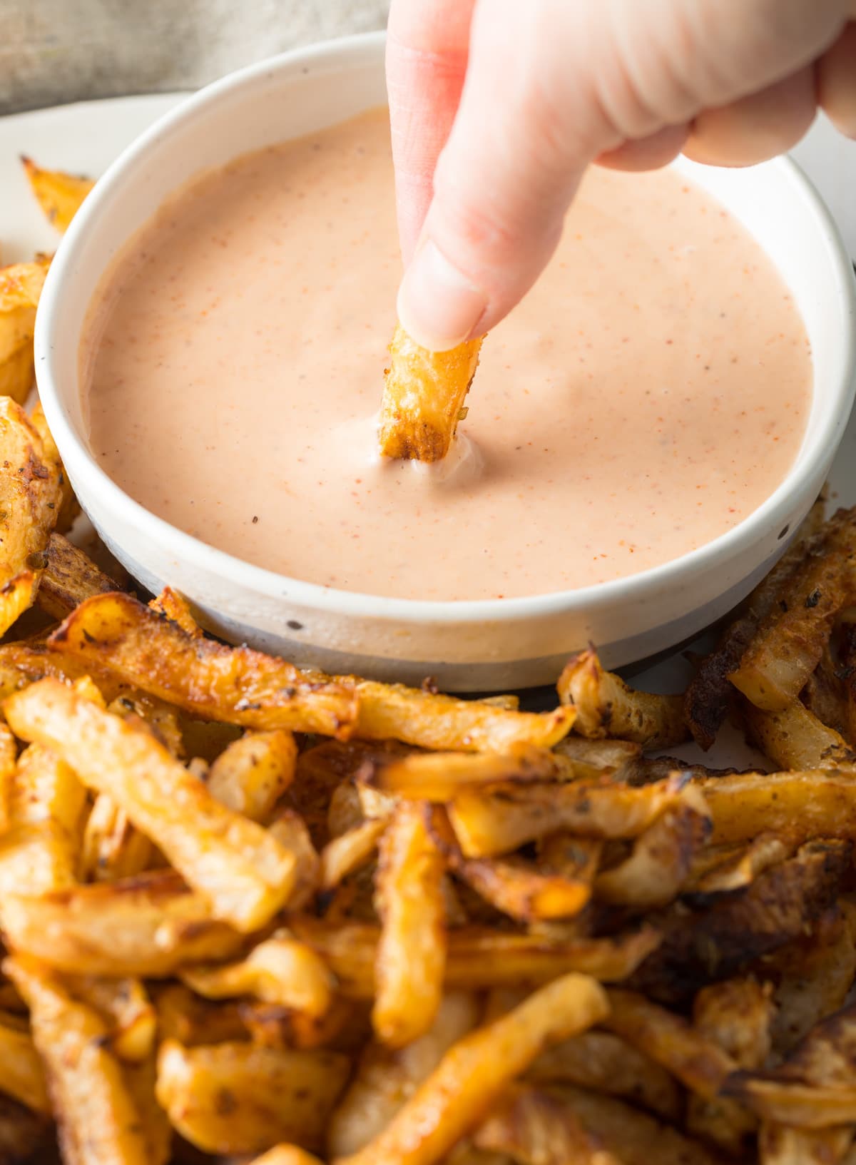 Hand dipping a turnip fry into a dipping sauce. 