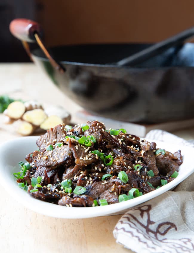 Korean beef bulgogi served in a white bowl with a black wok in the background.