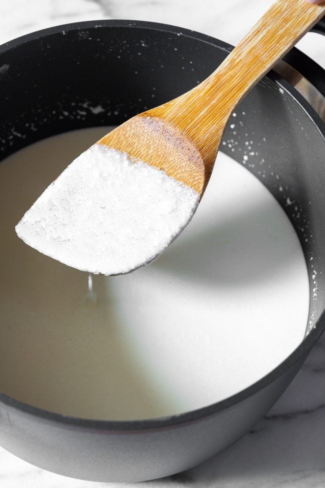 Stirring milk mixture with a wooden spoon in a metal pot.