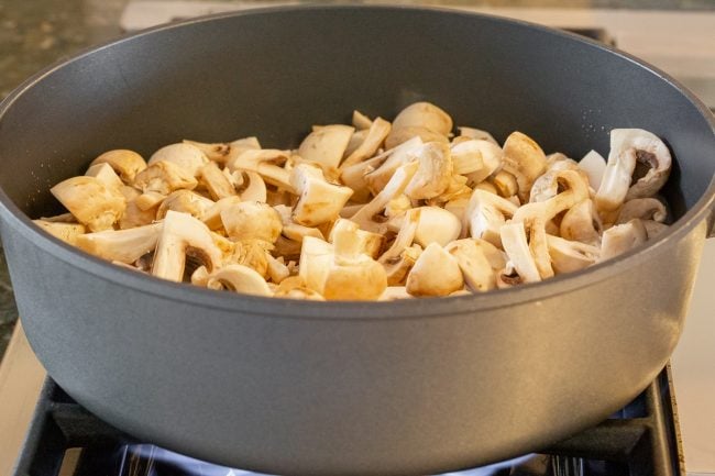 Diced mushrooms being cooked in a skillet on the stove. 