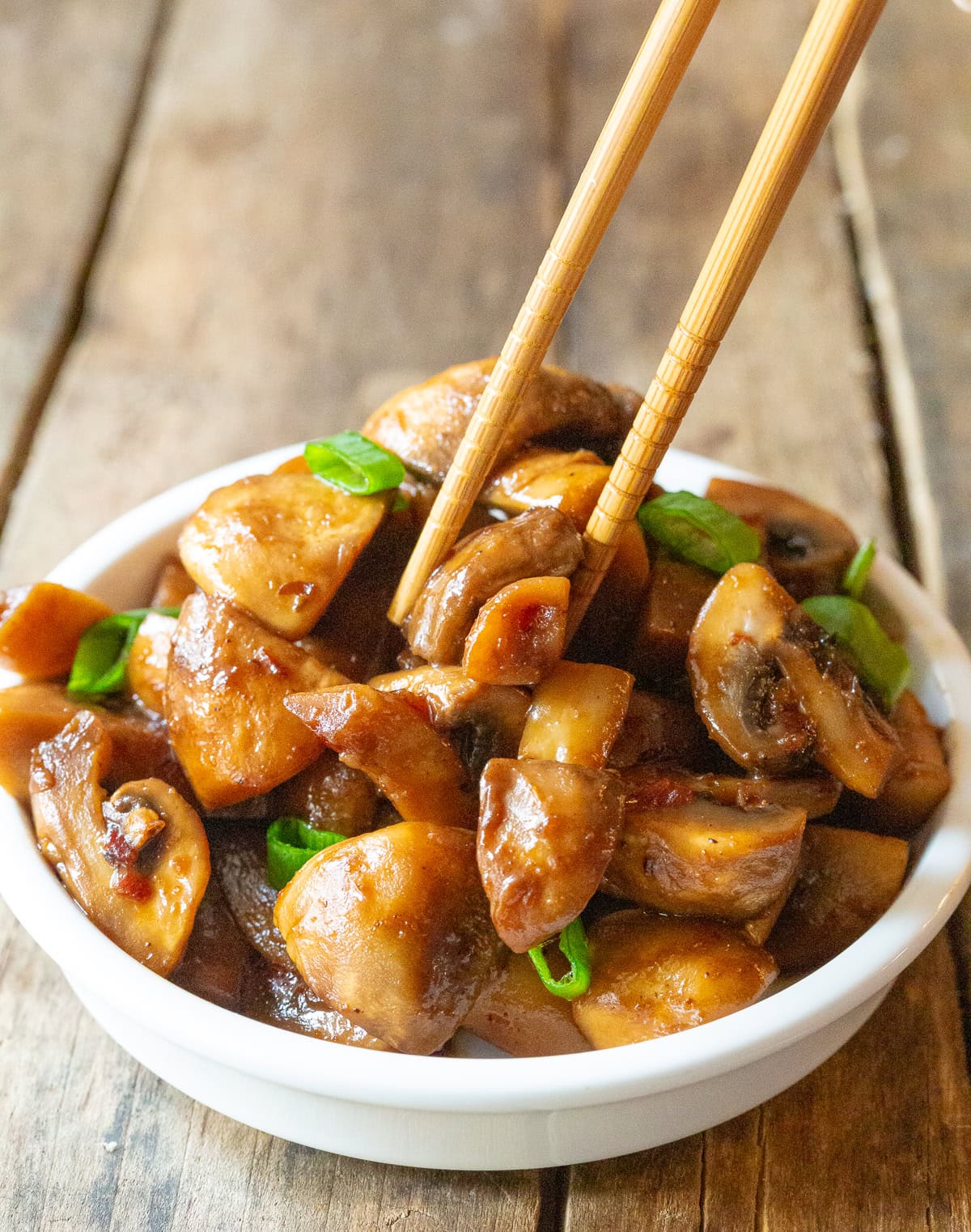 Chopsticks picking up a mushroom from the bowl. 