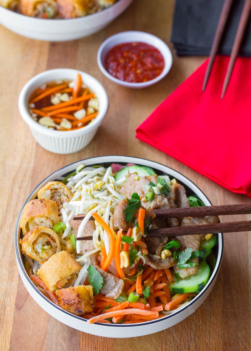 Chop sticks picking up a piece of pork and fresh veggies.