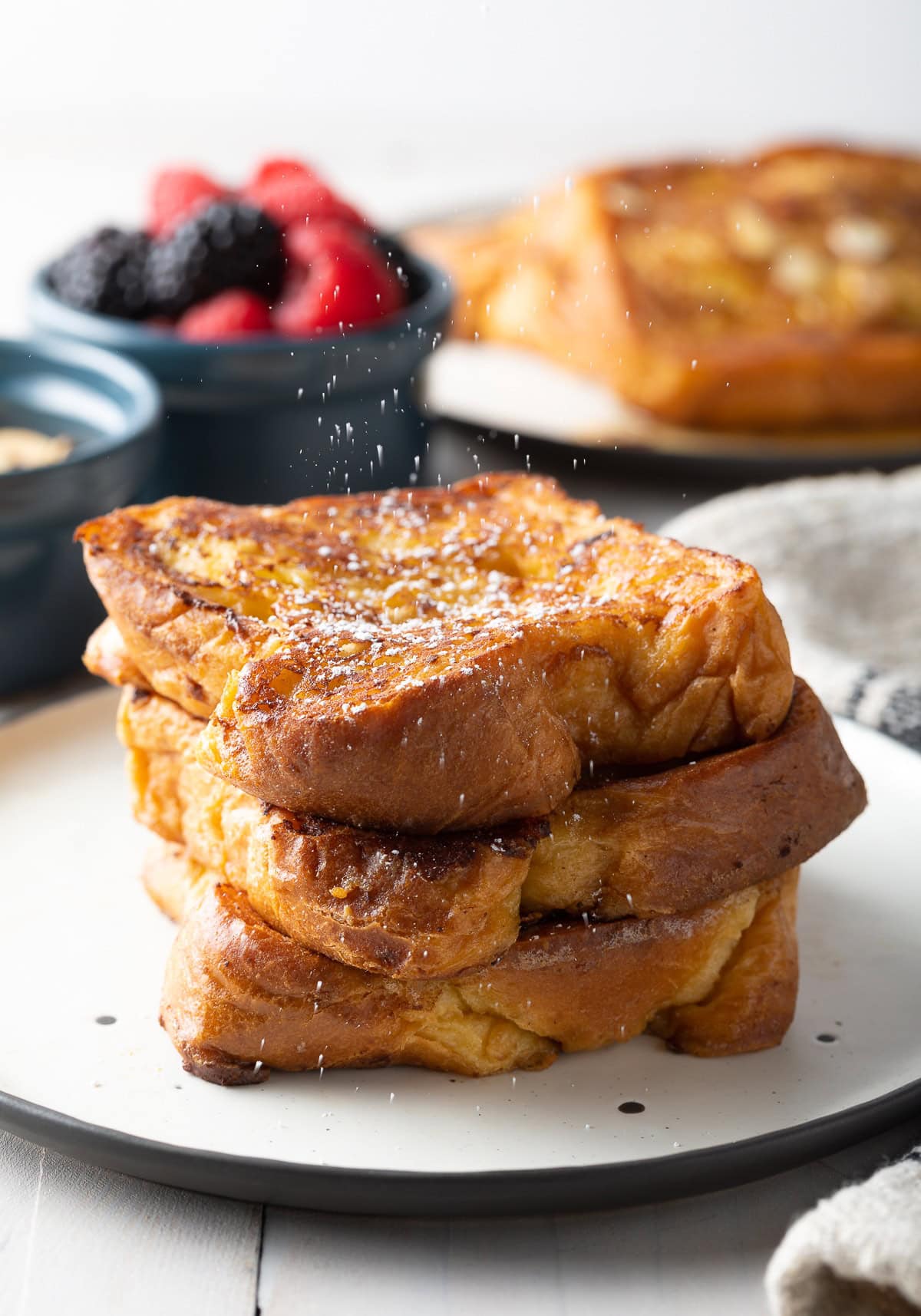 A stack of french toast on a white plate with powdered sugar dusting the top.