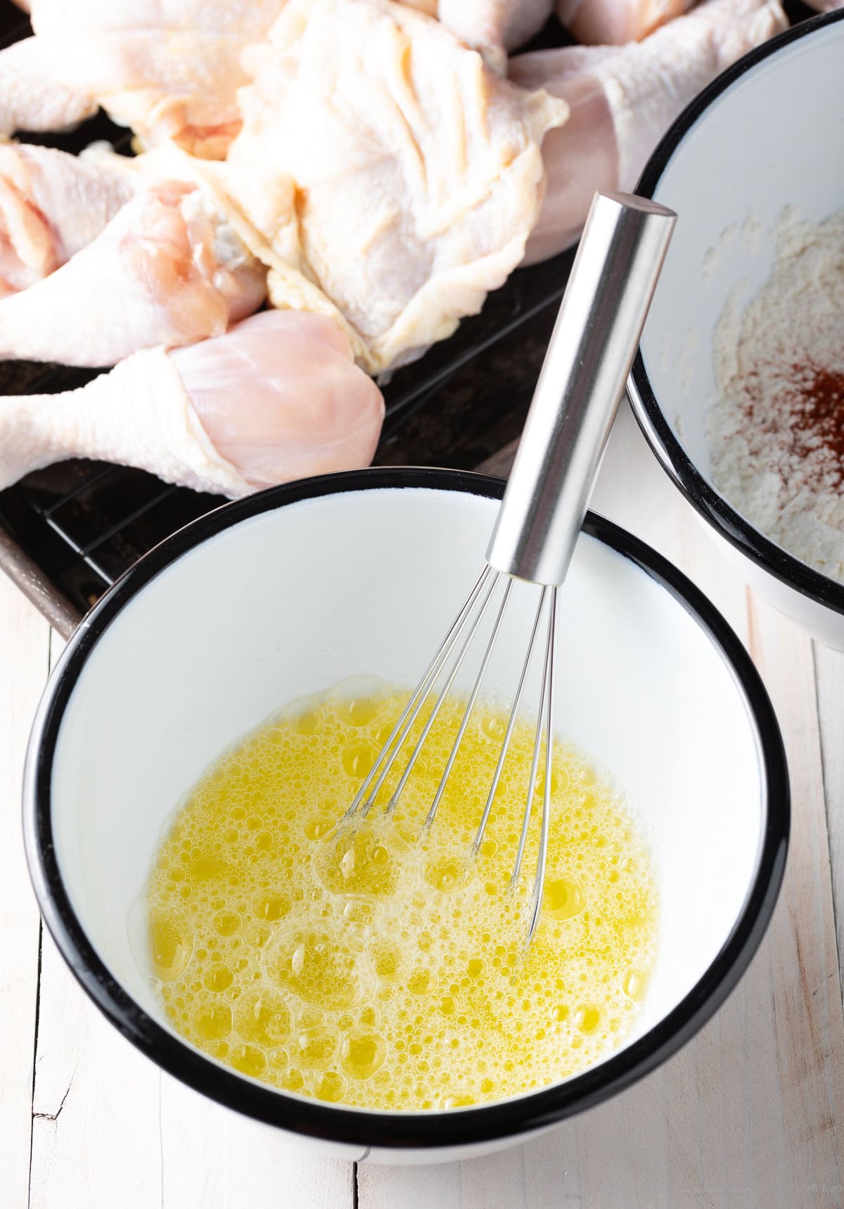 Egg whites frothy in a white mixing bowl with metal whisk.