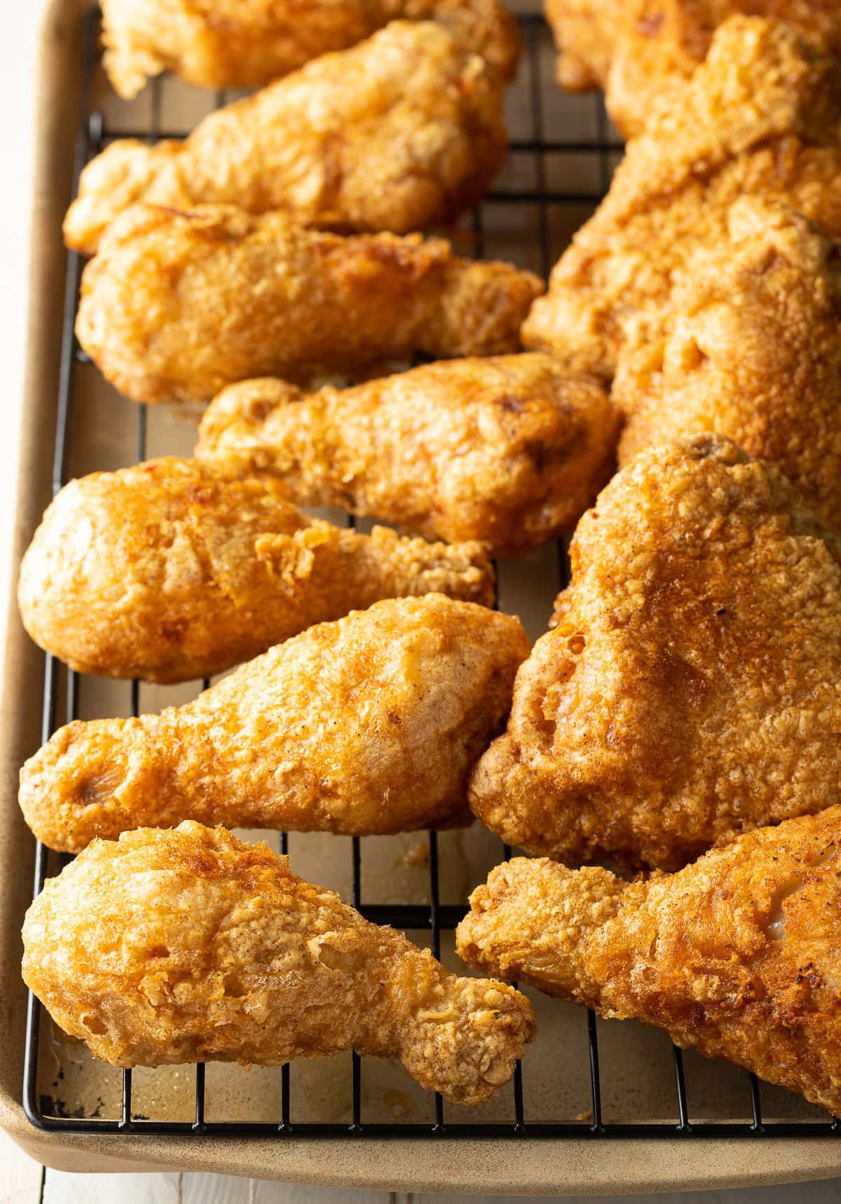 Several pieces of fried chicken legs and thighs on a wire rack over a baking sheet.