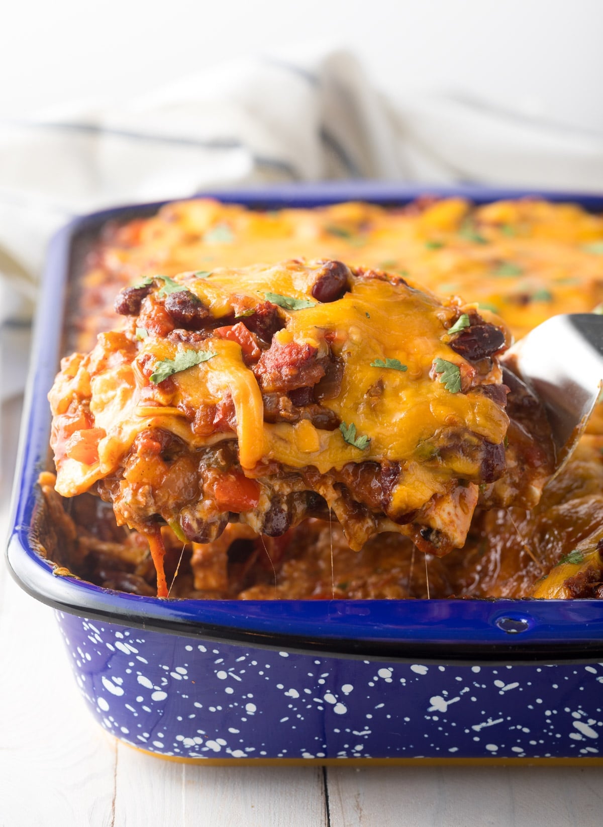 Easy Chili Lasagna lifted out of pan with cheese, beans, meat, and sauce.