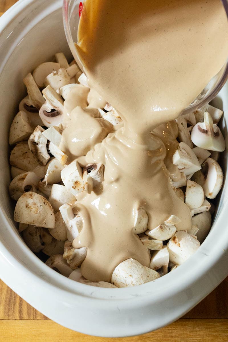 Mushrooms and Base #ASpicyPerspective #Beef #Stroganoff #BeefStroganoff #BeefStroganoffRecipe #SlowCookerBeefStroganoff #BeefStroganoffCrockpot #SlowCooker #Crockpot Stroganoff sauce being poured over mushrooms.