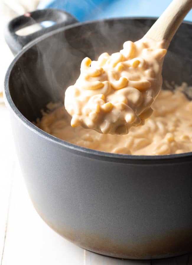 Steaming pot of homemade macaroni with a wooden spoon full of pasta 
