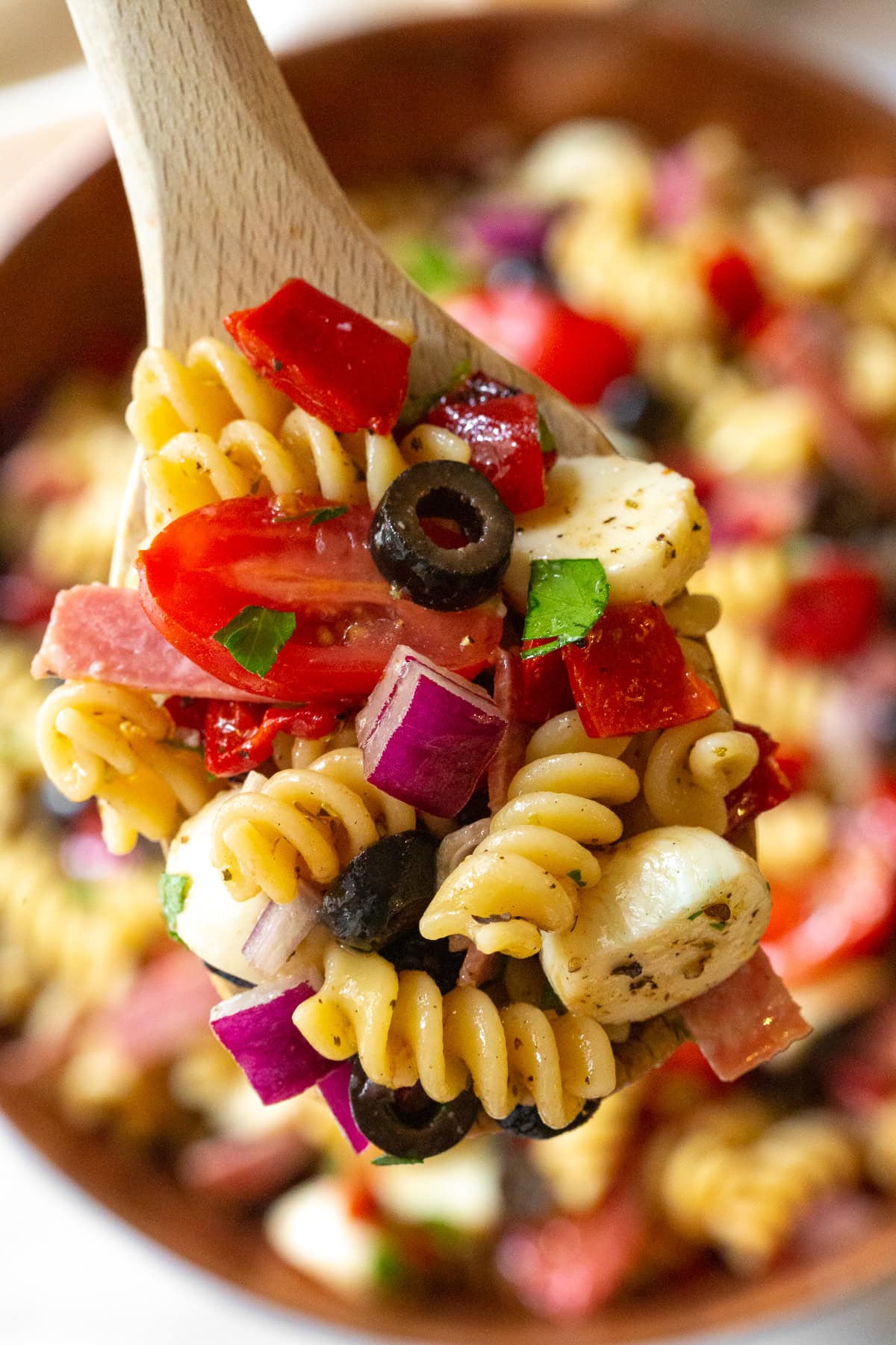 Wooden spoon with scoop of pasta salad on it.
