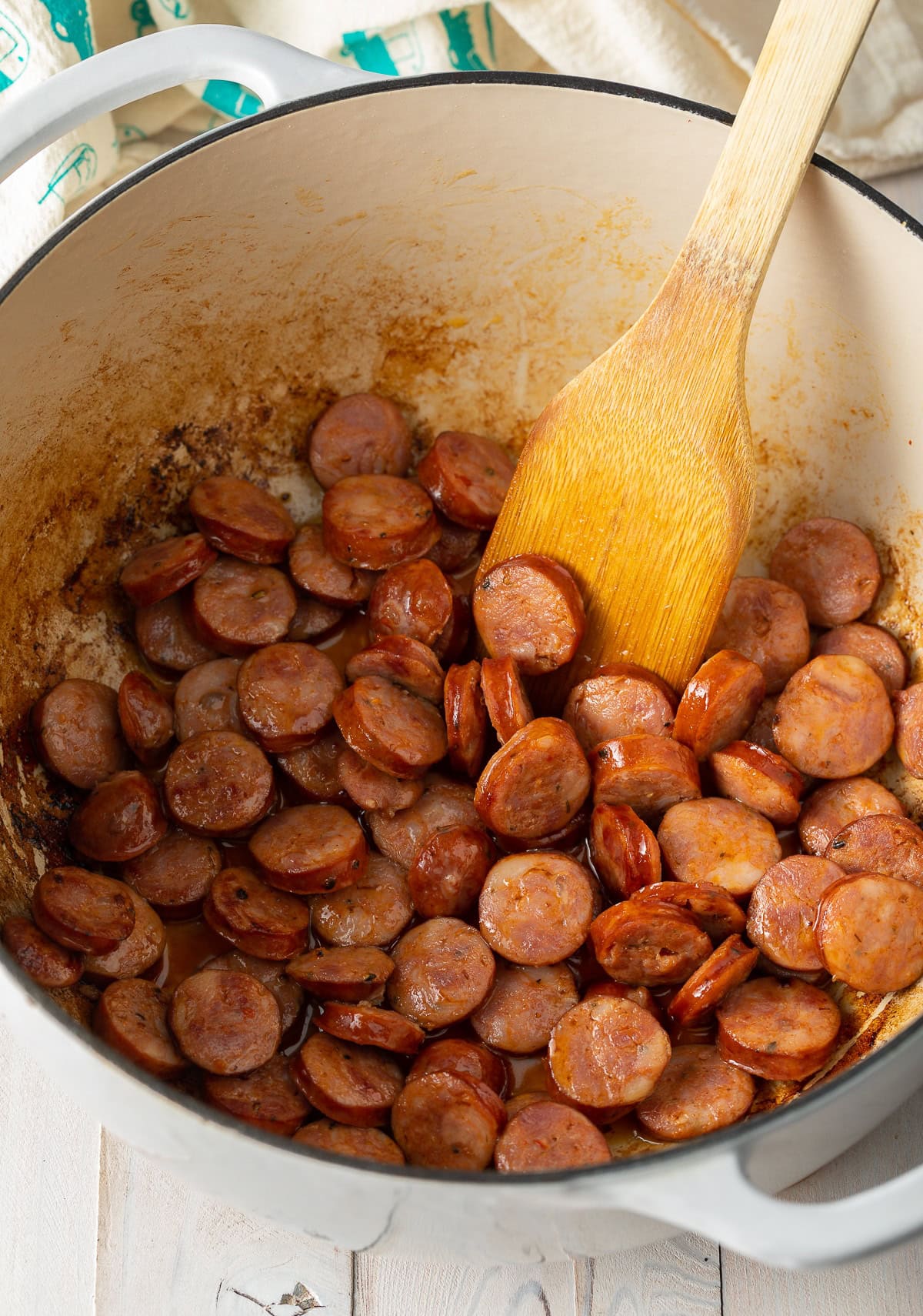 Sliced sausage in a pot with a wooden spoon.