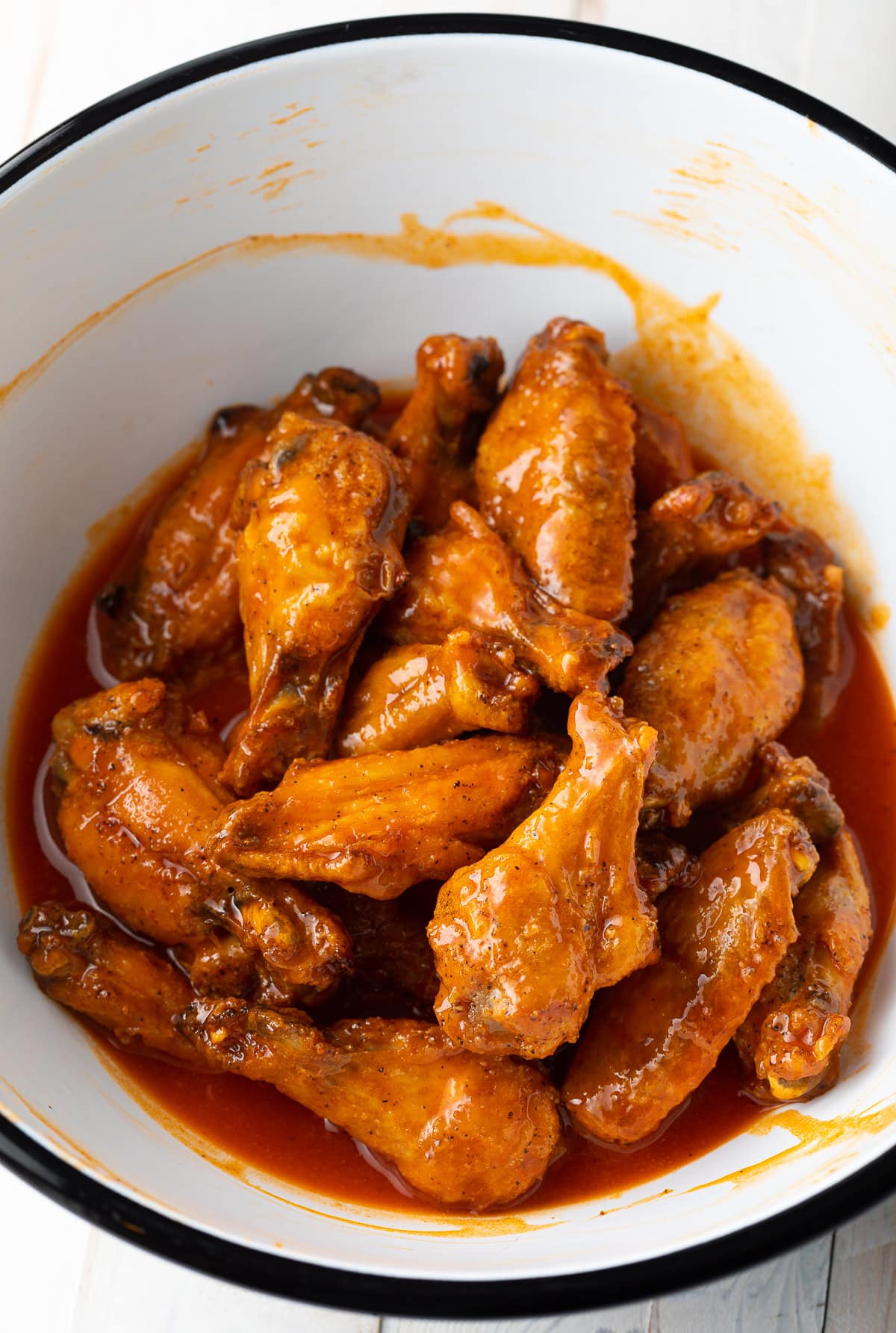 White mixing bowl tossing chicken wings in buffalo sauce.