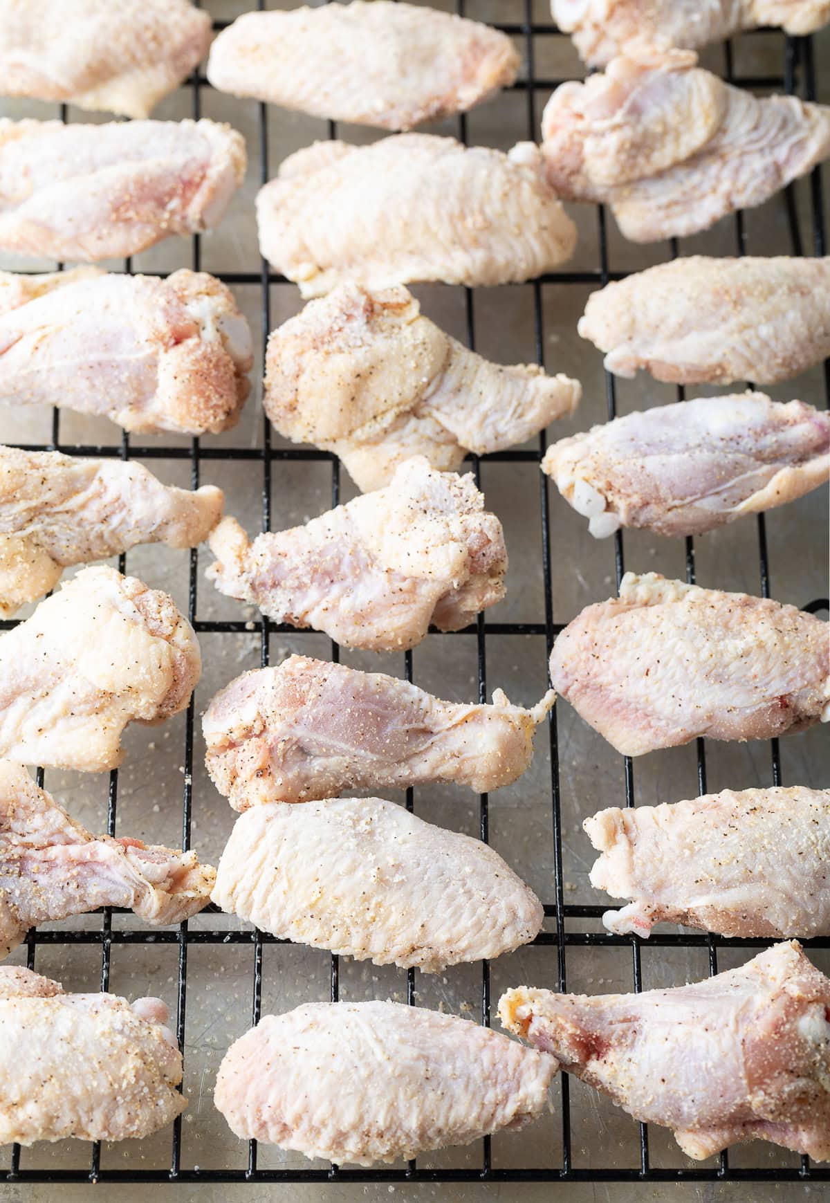 Raw chicken wings and drummies on a wire rack.