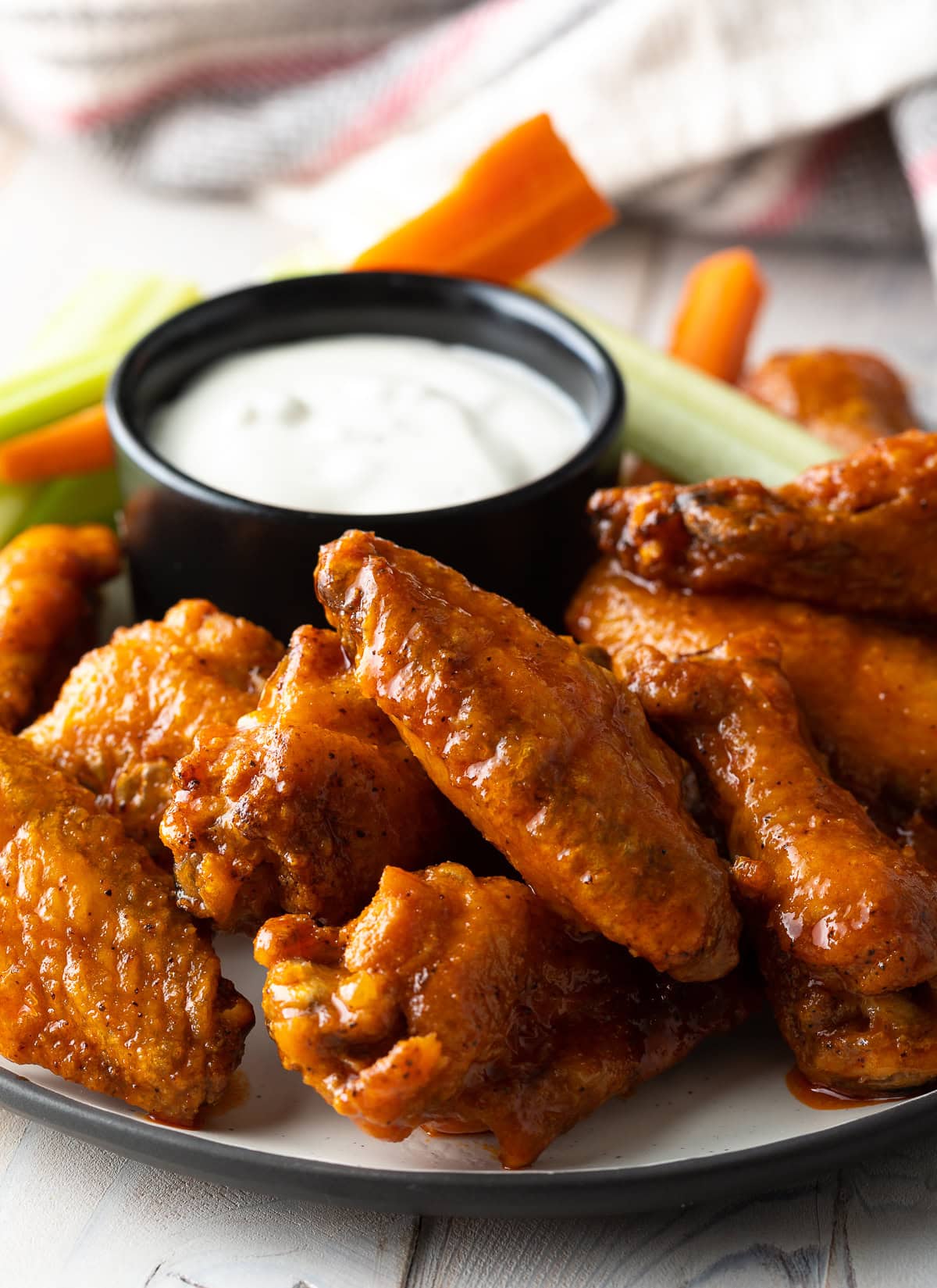 Plateful of oven baked chicken wings with black ramekin of ranch dressing, carrot sticks and celery sticks.