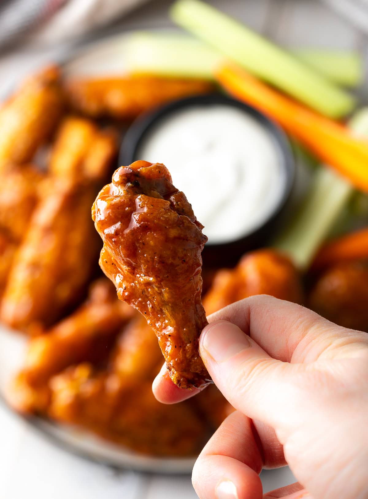 Hand holding a baked buffalo chicken wing drummy to camera.
