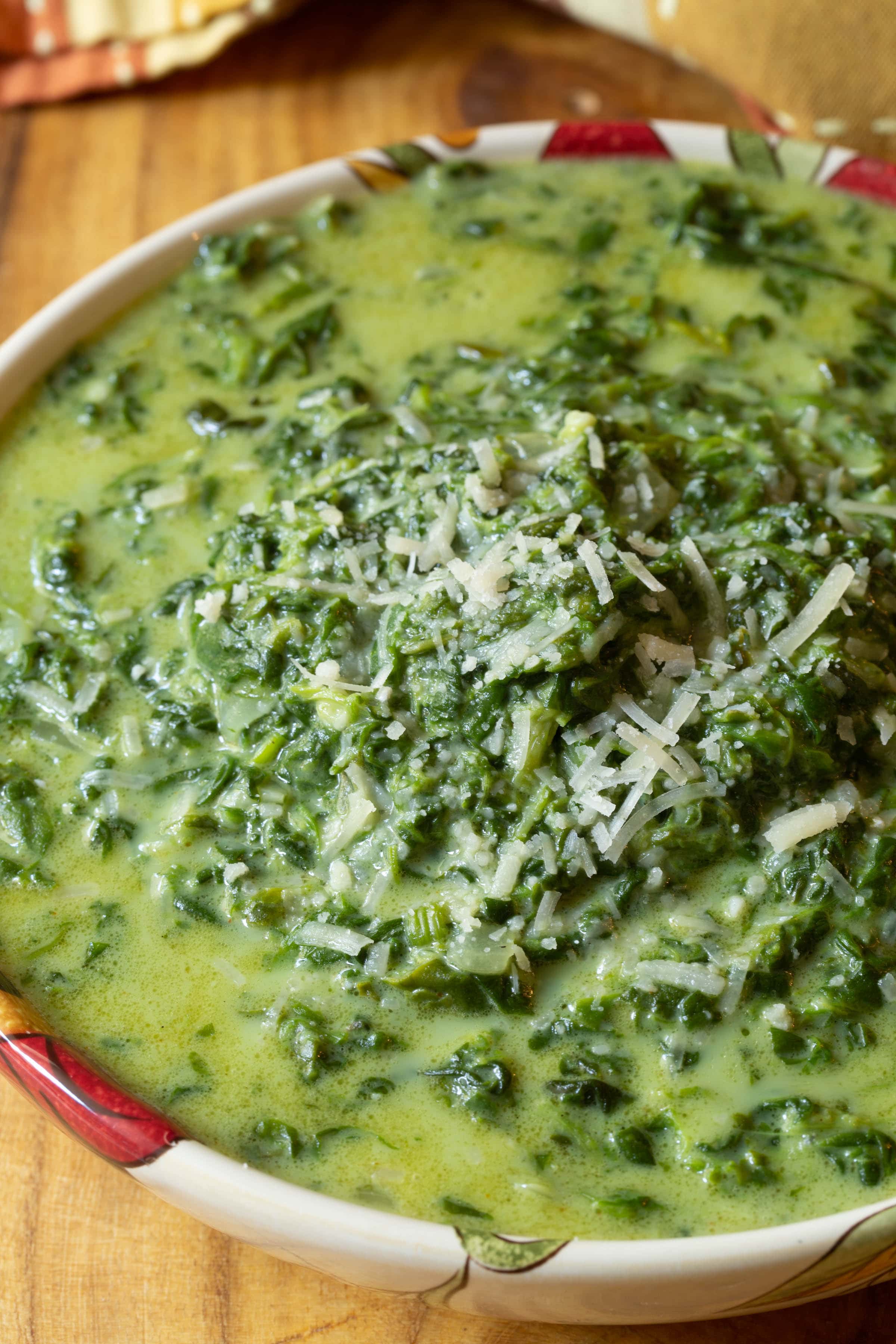 Slow Cooker Creamed Spinach with some cheese sprinkled on top in a serving bowl.