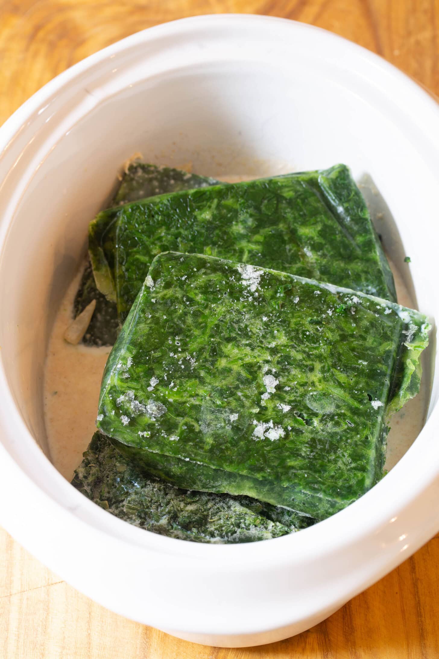 Frozen Spinach is placed in the slow cooker on top of the onions and cream mixture.