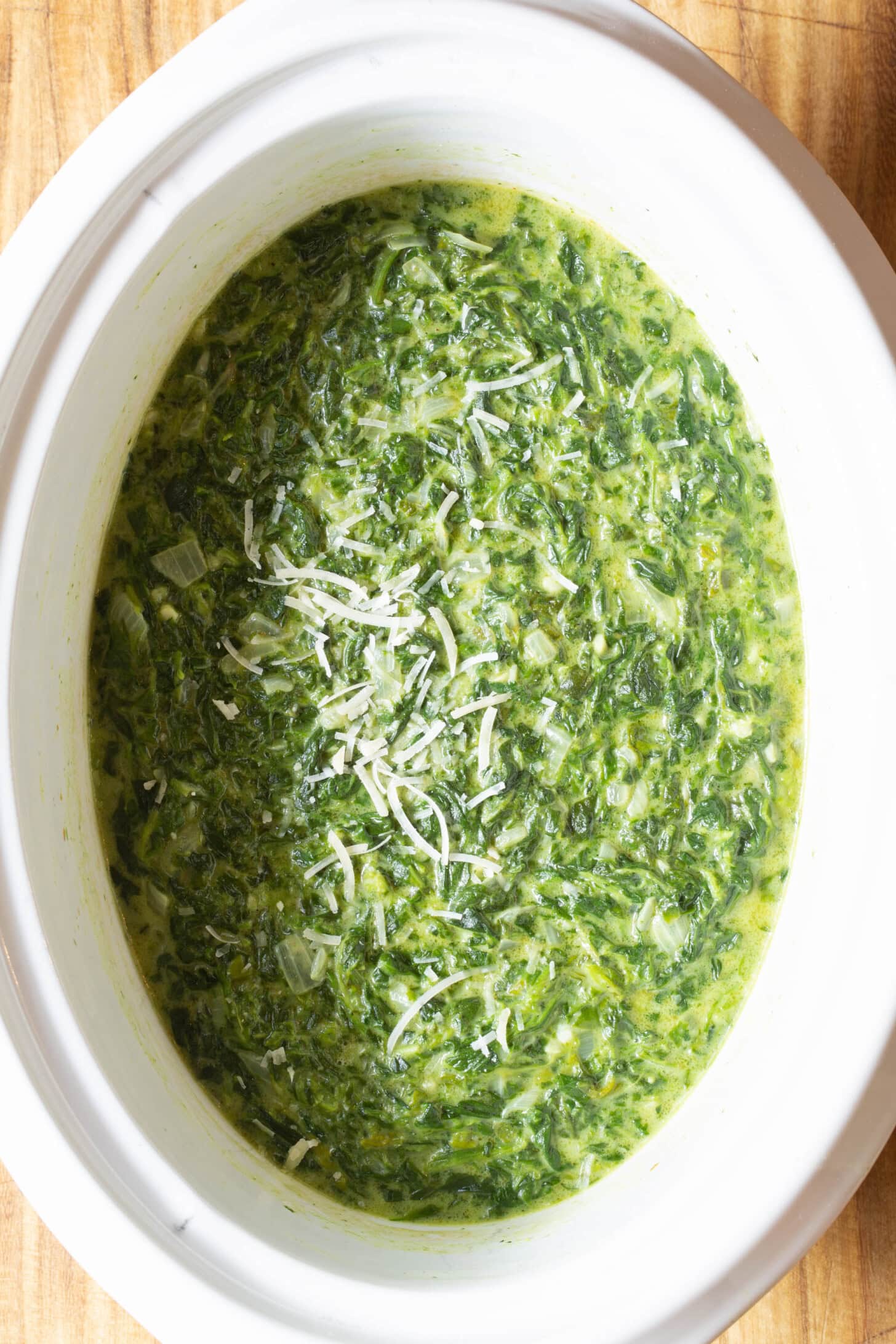 Crockpot with loaded creamy spinach topped with grated parmesan.