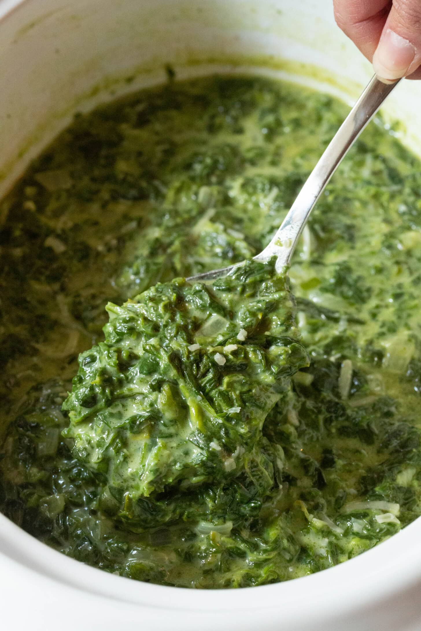 Creamed spinach in a crock pot with a large spoon taking a scoop.